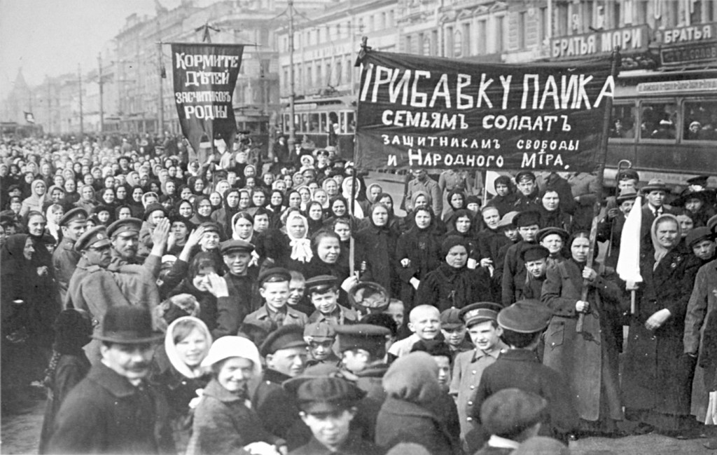 Demonstration from 1917. Women and  men hold banners with Cyrillic writing. The street is crowded. There are children in the foreground.