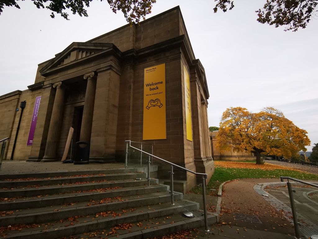 Shieffled's Weston Park Museum. A large stone building, fronted by column and accessed via raised steps. The scene is autumnal. 